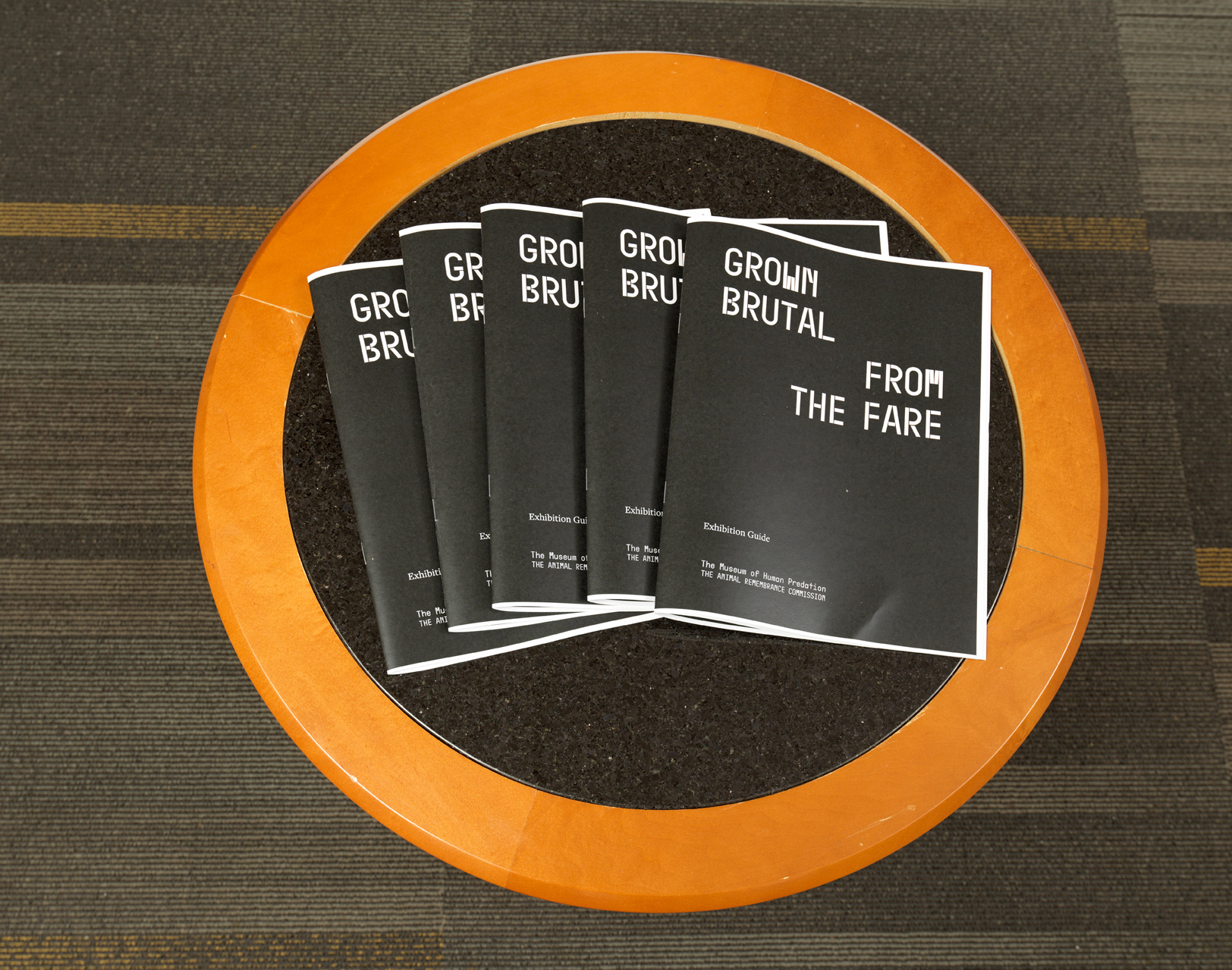 Several booklets on the exhibit, Grown Brutal From the Fare, displayed on a round table