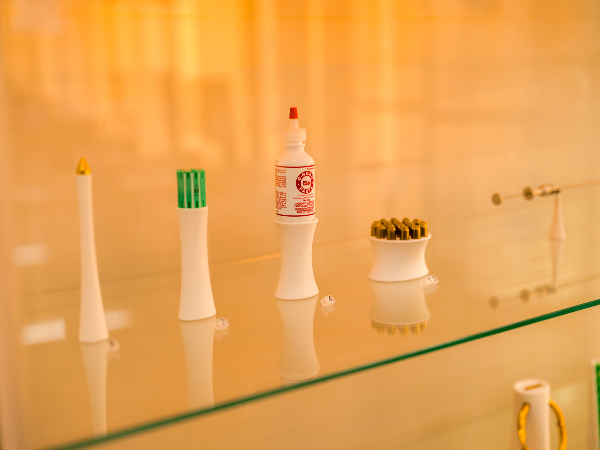 Close up of artifacts in the vitrine including an electric prod tip, a growth hormone cartridge, de-horning paste, and killing cartridges.