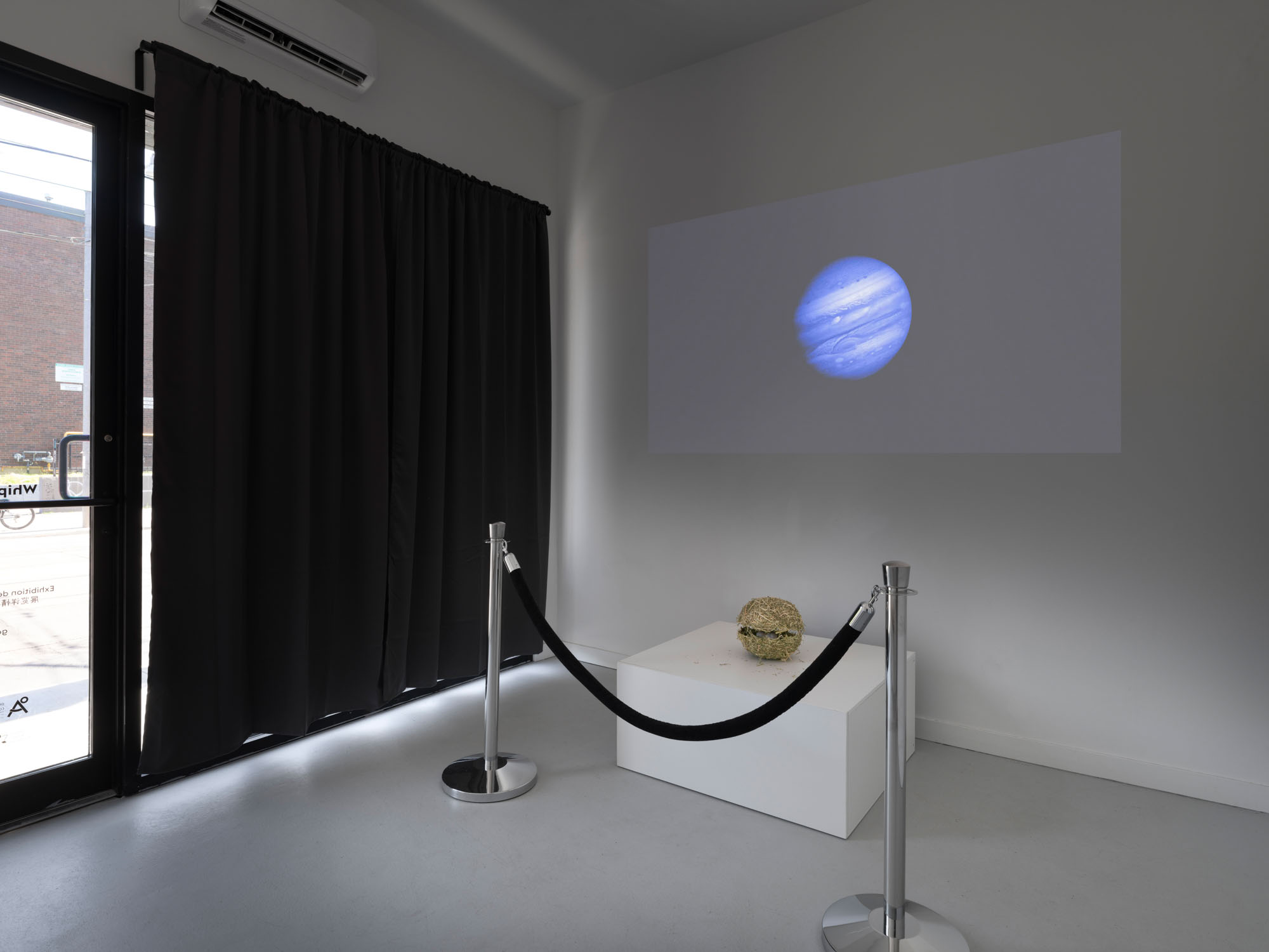 Hay sphere behind a velvet rope with a projection of Jupiter in the background